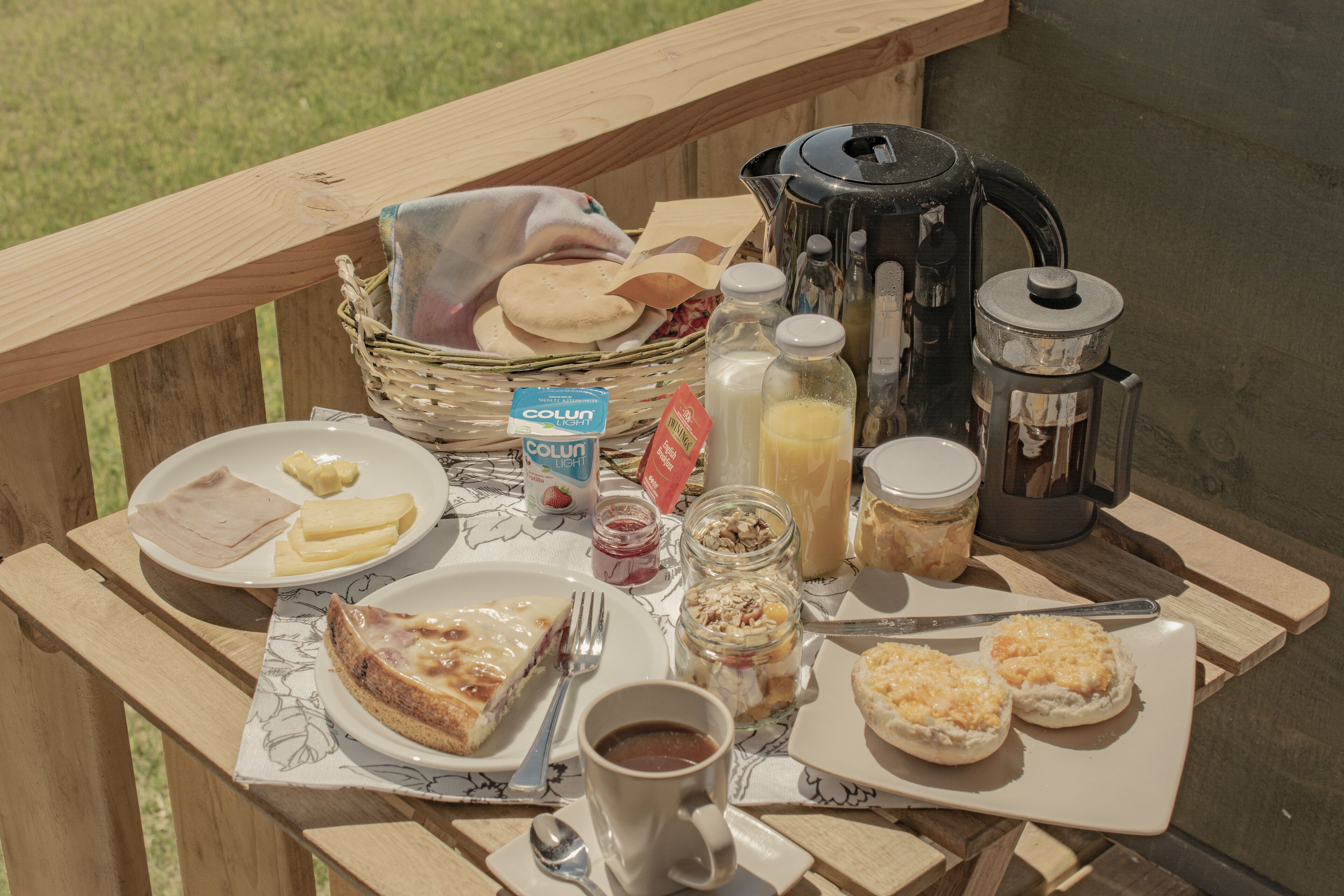 Ein Picknick auf einer Holzterrasse mit verschiedenen Speisen, darunter Sandwiches, Gebäck und einer Kaffeekanne.