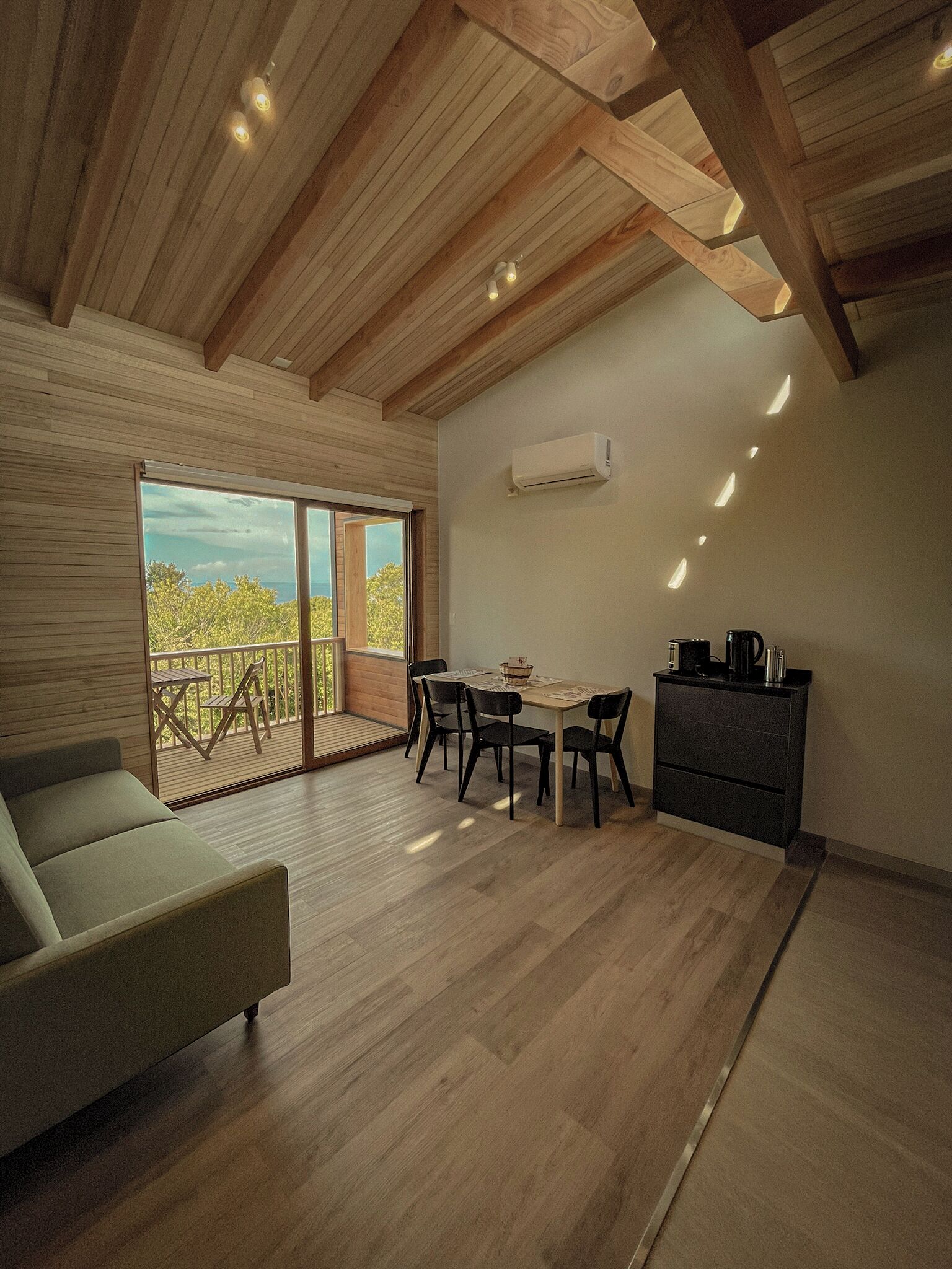 A spacious room with a wooden ceiling, a balcony with a view, a dining area, and a seating area.