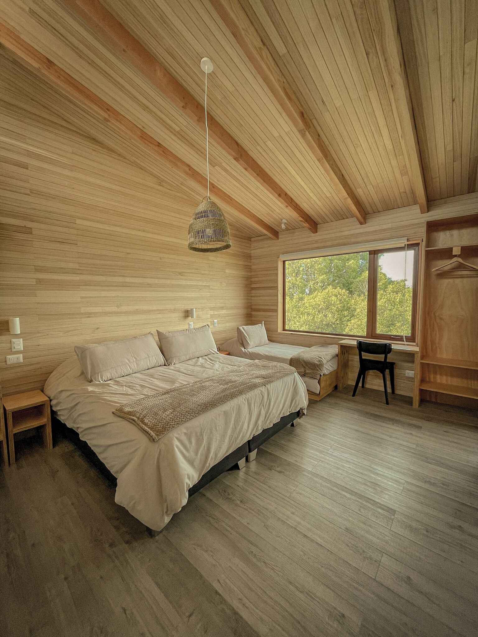 A bedroom with a large bed, a desk, and a chair. There is a window with a view of trees.