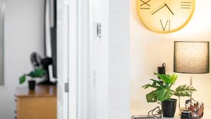 En gang med en dør, der fører til et værelse, et vægur og en lampe med en plante.