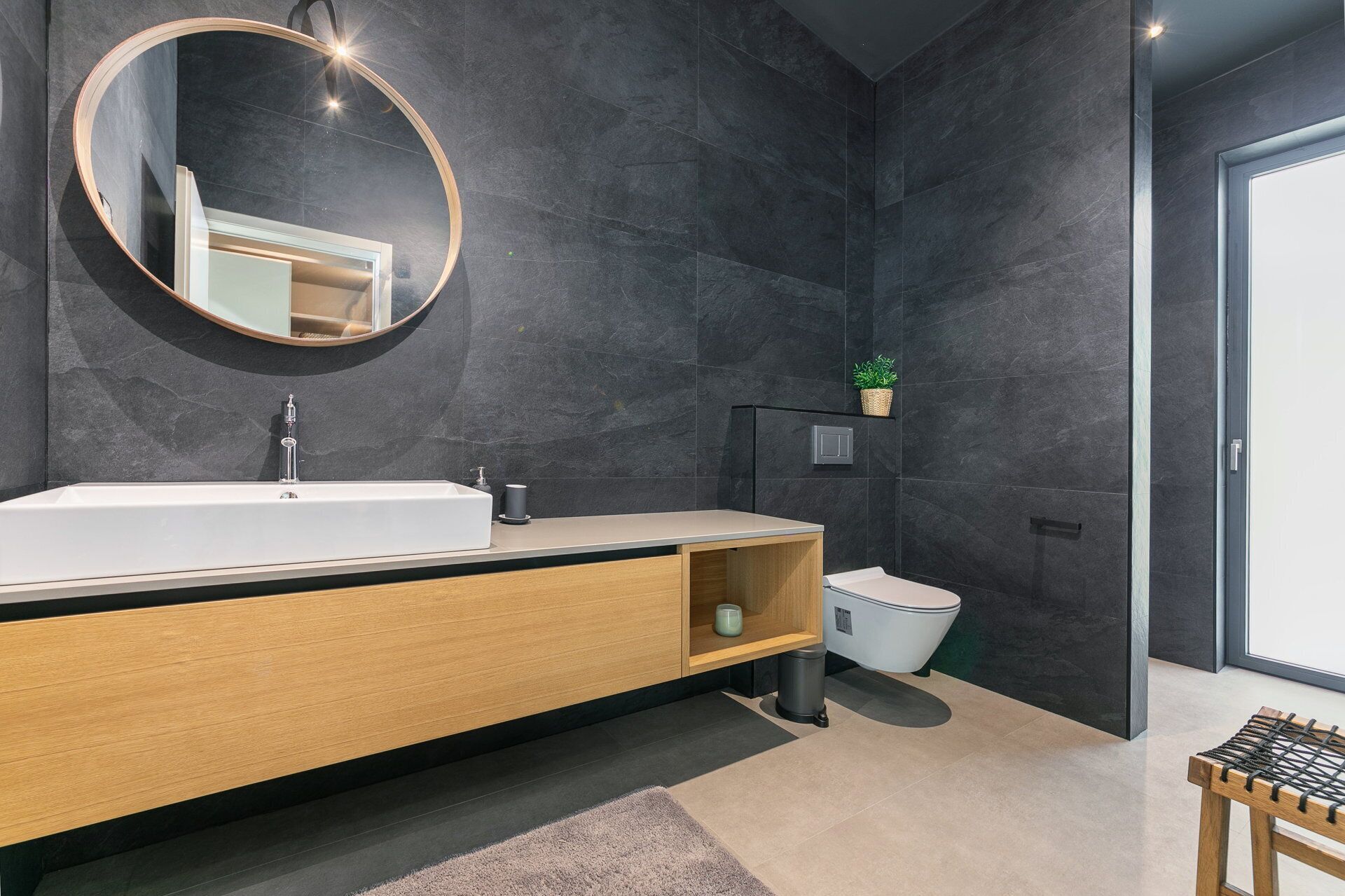Une salle de bain moderne avec un grand lavabo, un miroir et des murs recouverts de carreaux de couleur foncée.