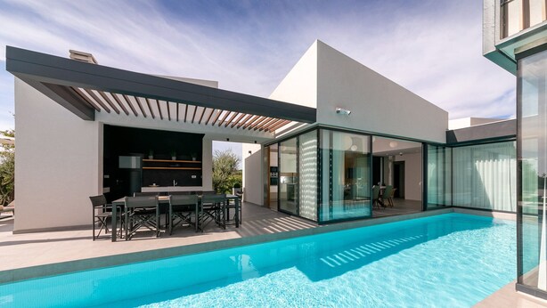 Una casa moderna con piscina, zona de comedor exterior y un espacio con paredes de vidrio.