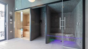 Un baño moderno con cabina de vidrio, sauna de madera y zona de ducha con pared de diseño tipo cuadrícula.