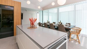 Una cocina moderna con una isla central, comedor con sillas y ventanas amplias.