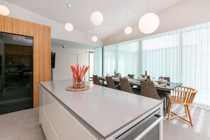 Eine moderne Küche mit einer zentralen Kochinsel, einem Essbereich mit Stühlen und großen Fenstern.