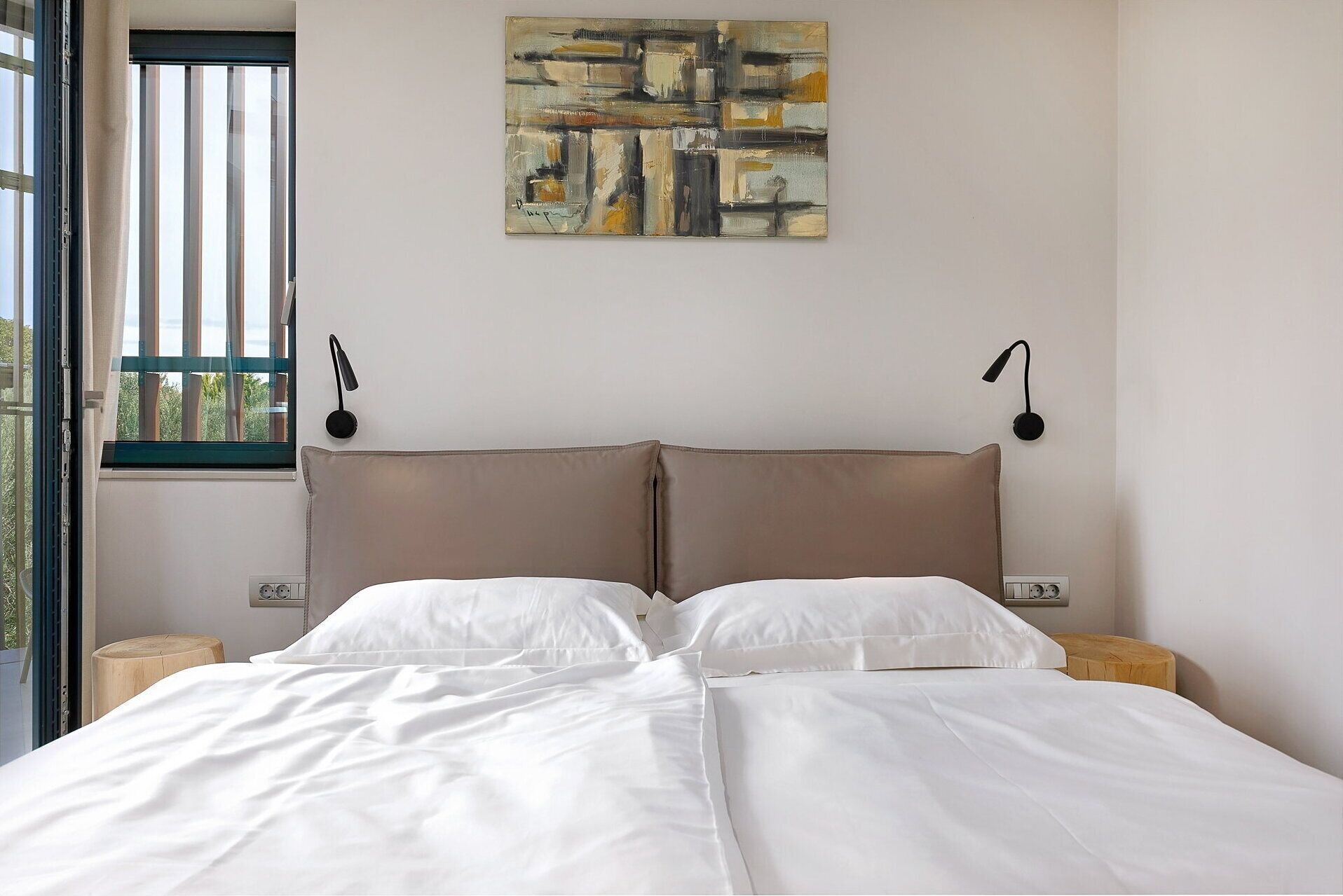 A bedroom with a bed, two bedside tables, a wall-mounted lamp, and a window with blinds.
