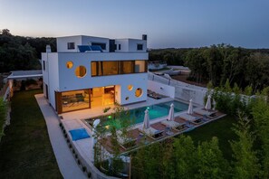 A modern two-story house with a swimming pool, large windows, and a well-maintained garden.