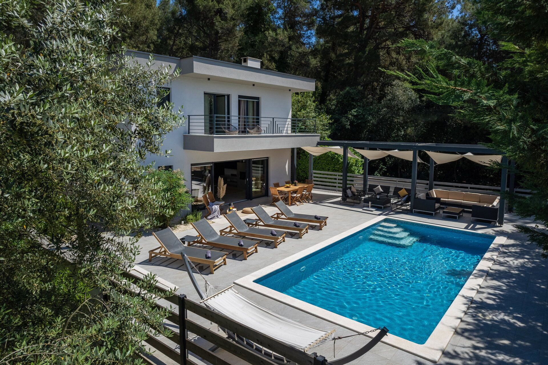 Et moderne hus med to etager, en swimmingpool, udendørs siddepladser og en overdækket terrasse.