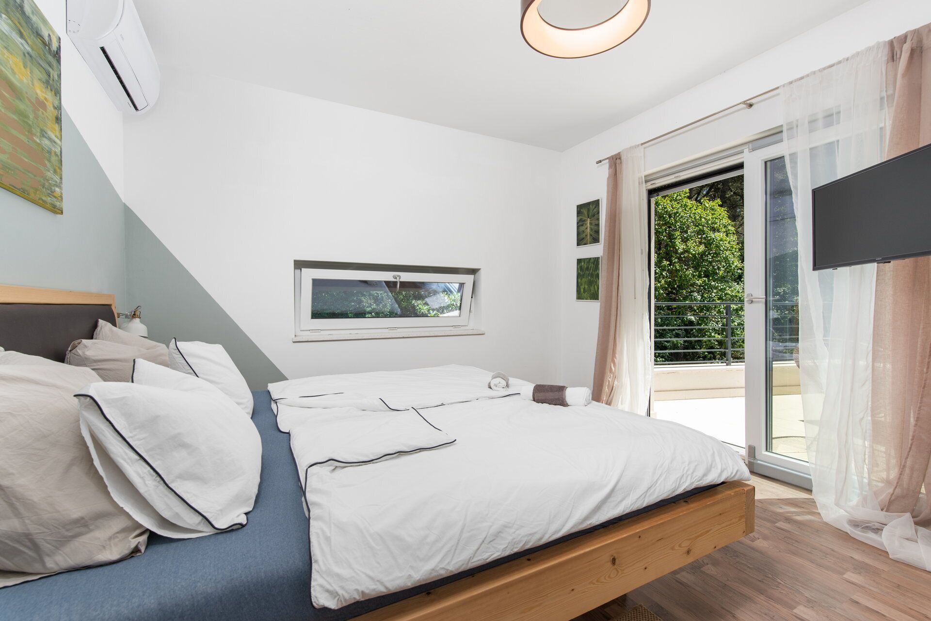 A bedroom with a bed, a window, and a view of greenery outside.