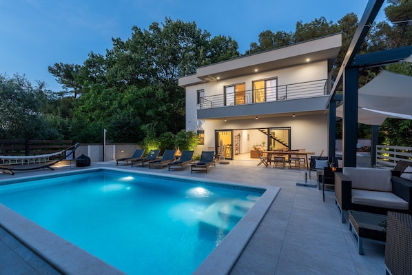 Une maison moderne à deux étages dotée d’une piscine, d’un espace salon extérieur et d’un patio couvert.
