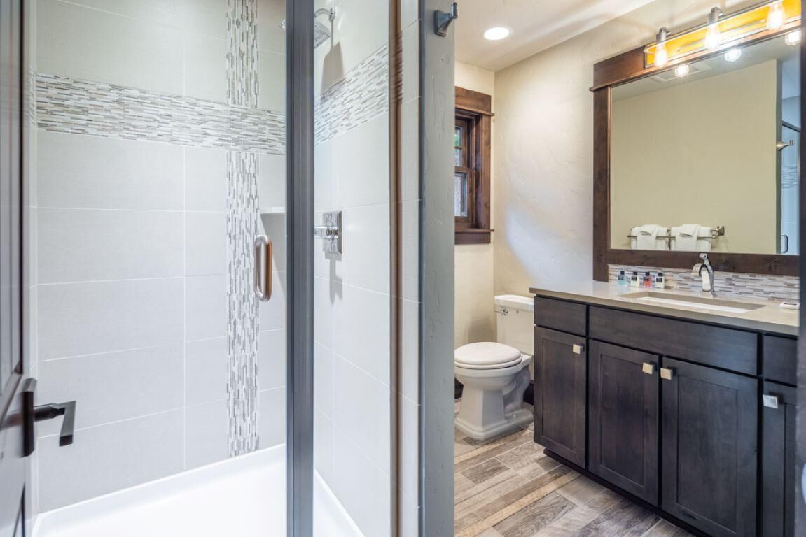 A modern bathroom with a glass-enclosed shower, a white toilet, dark wooden cabinets, and a large mirror with lights.