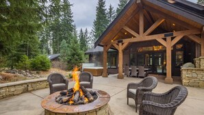 A stone fire pit with burning logs, surrounded by wicker chairs.