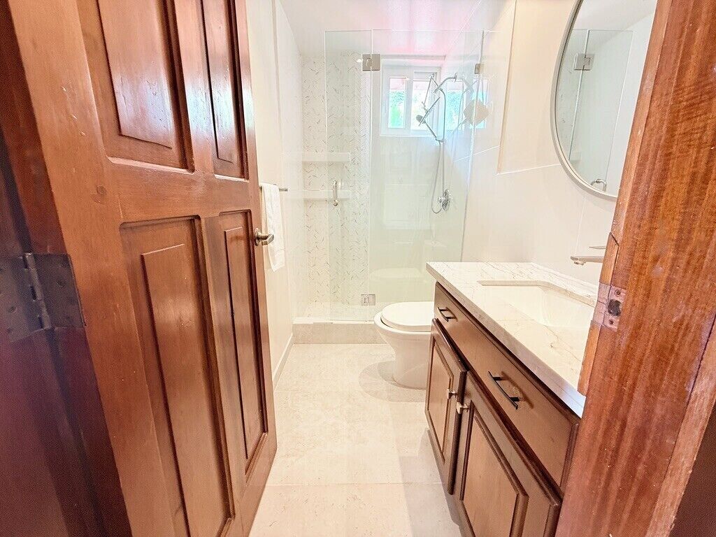 A bathroom with a shower, toilet, and wooden cabinets.