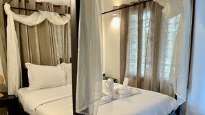 Una cama con dosel cubierta con sábanas blancas y un dosel, una mesita de noche con lámpara, y vistas al exterior a través de cortinas de gasa.
