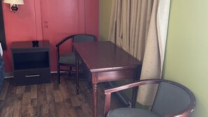A room with a wooden floor, a red door, a table with chairs, a lamp, and a curtain. - BUDGETINN (Monroeville)