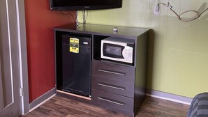 A compact room with a flat-screen TV mounted on a cabinet, a microwave, and a small refrigerator. - BUDGETINN (Monroeville)