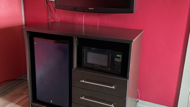A kitchenette with a microwave, a small refrigerator, and a flat-screen TV mounted above the counter. - BUDGETINN (Monroeville)