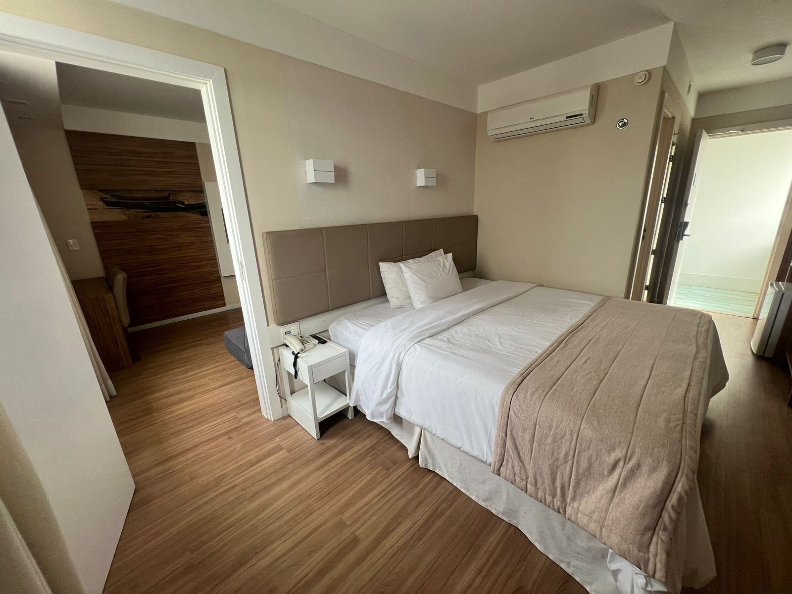 A hotel room with a large bed, bedside tables, a wardrobe, and an air conditioning unit.