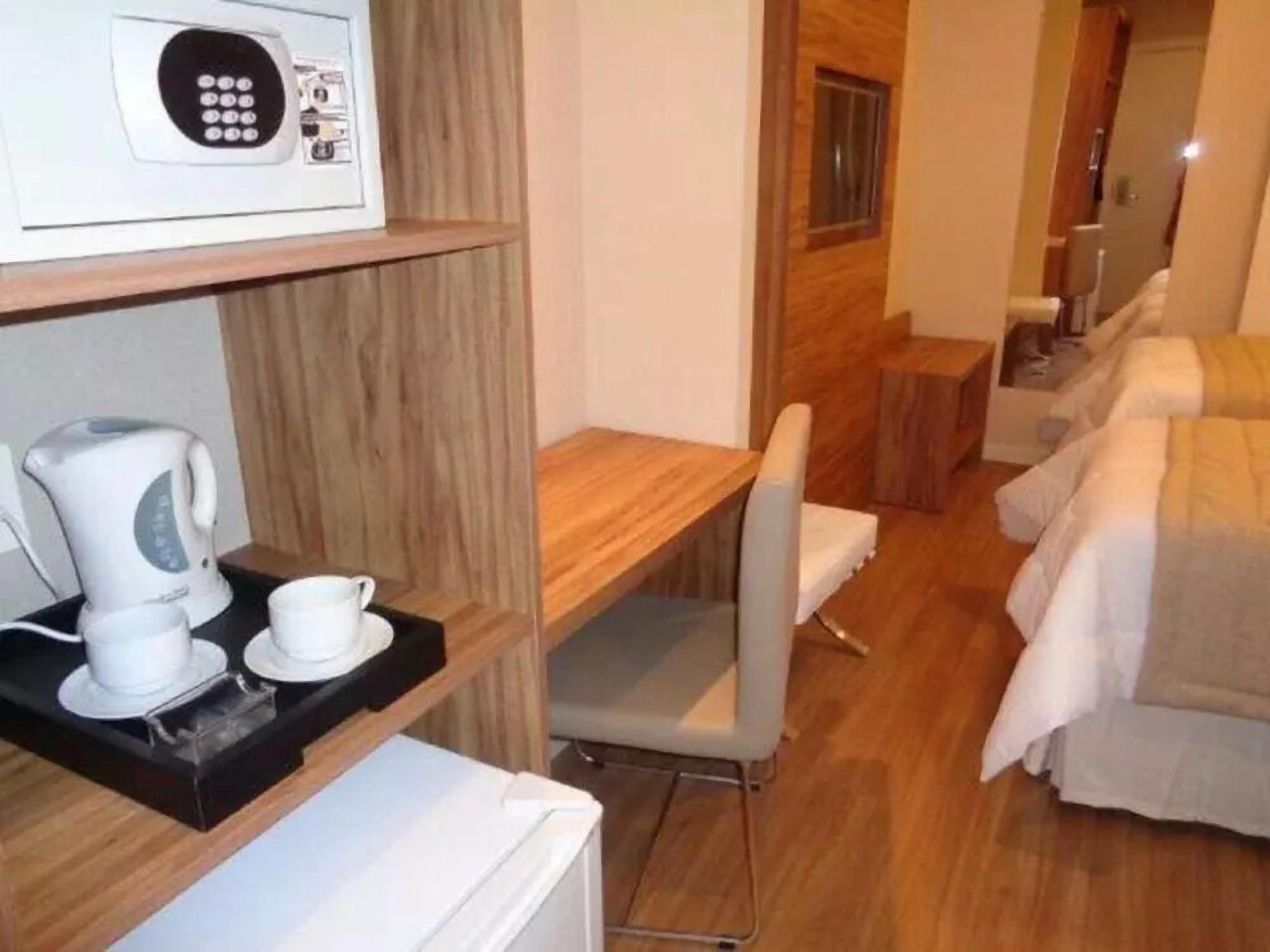Habitación de hotel con piso de madera, una cama con ropa blanca, un escritorio pequeño con una silla, un microondas y un hervidor en una bandeja.