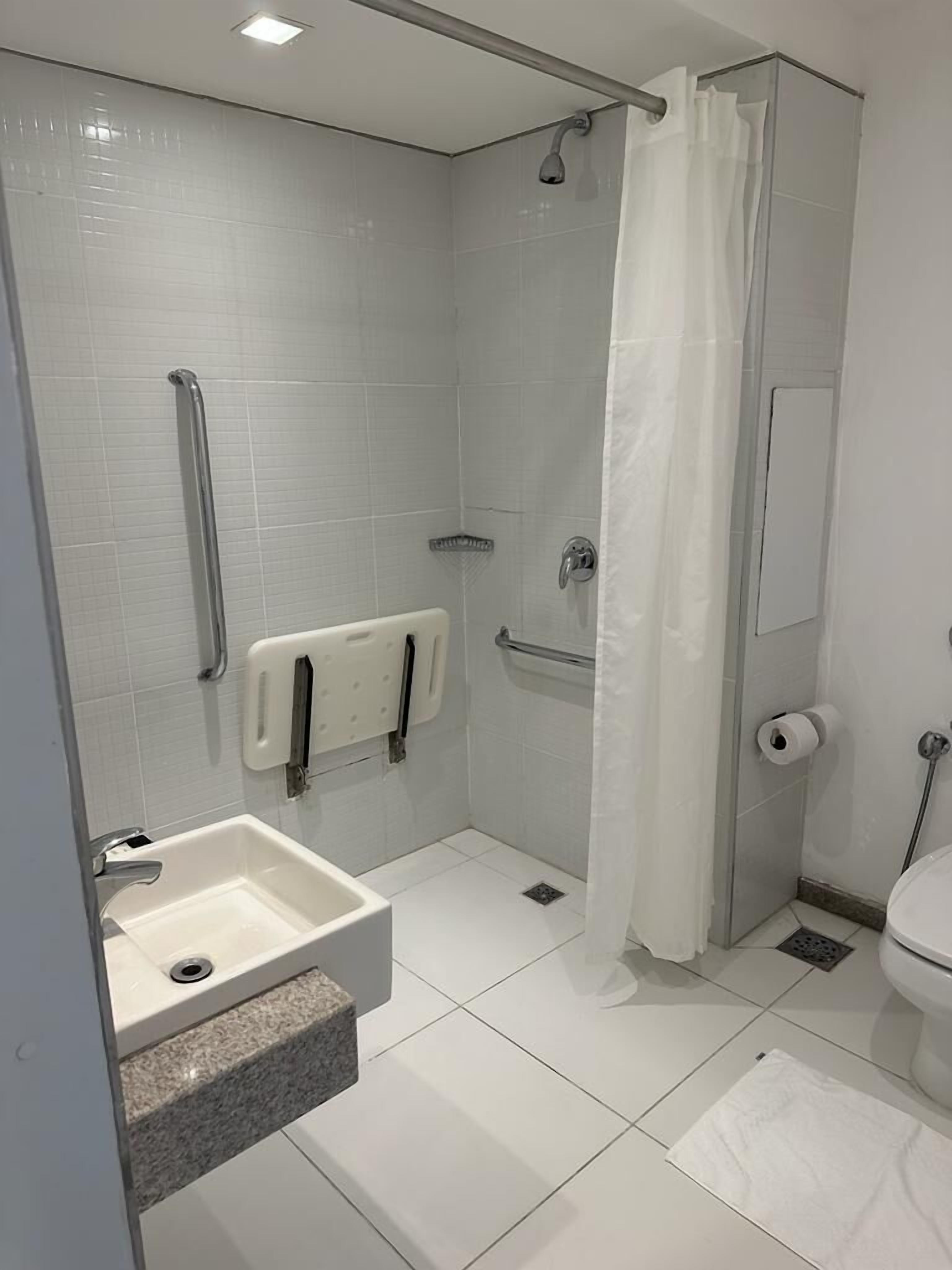 Uma casa de banho moderna com chuveiro de entrada livre, barras de apoio, lavatório embutido e sanita.