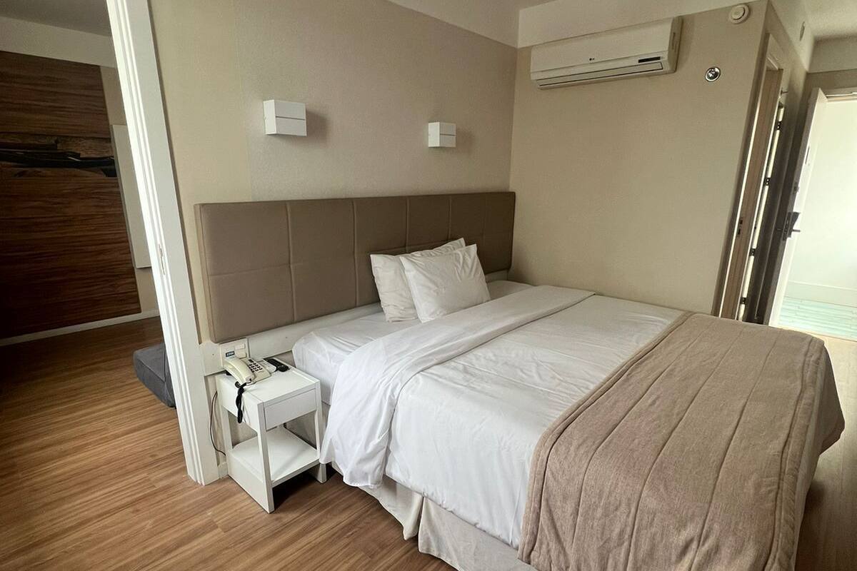 A hotel room with a large bed, a bedside table with a phone, and a wall-mounted air conditioner.