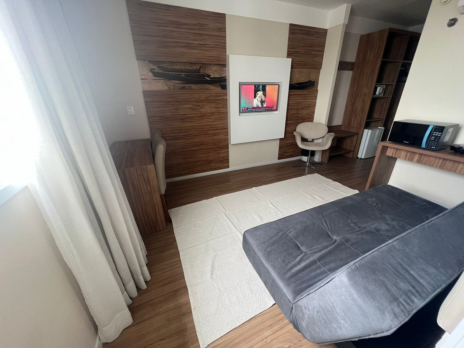 Un soggiorno moderno con un divano grigio, un tappeto bianco, pavimento in legno, una TV a parete e un piccolo armadietto in legno.