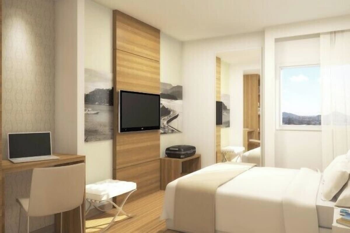 A modern hotel room with a bed, desk, chair, television, and artwork on the walls.