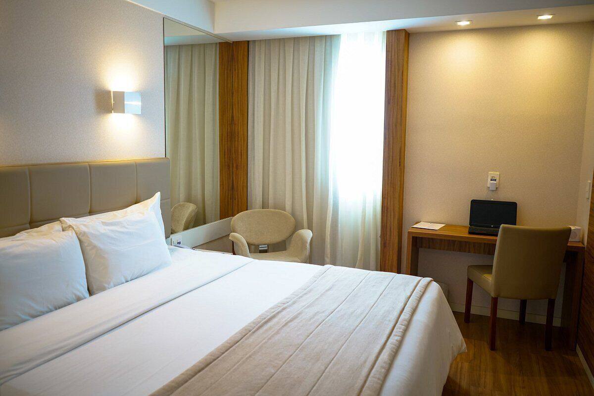 A hotel room with a large bed, a desk with a laptop, a chair, and a mirror.