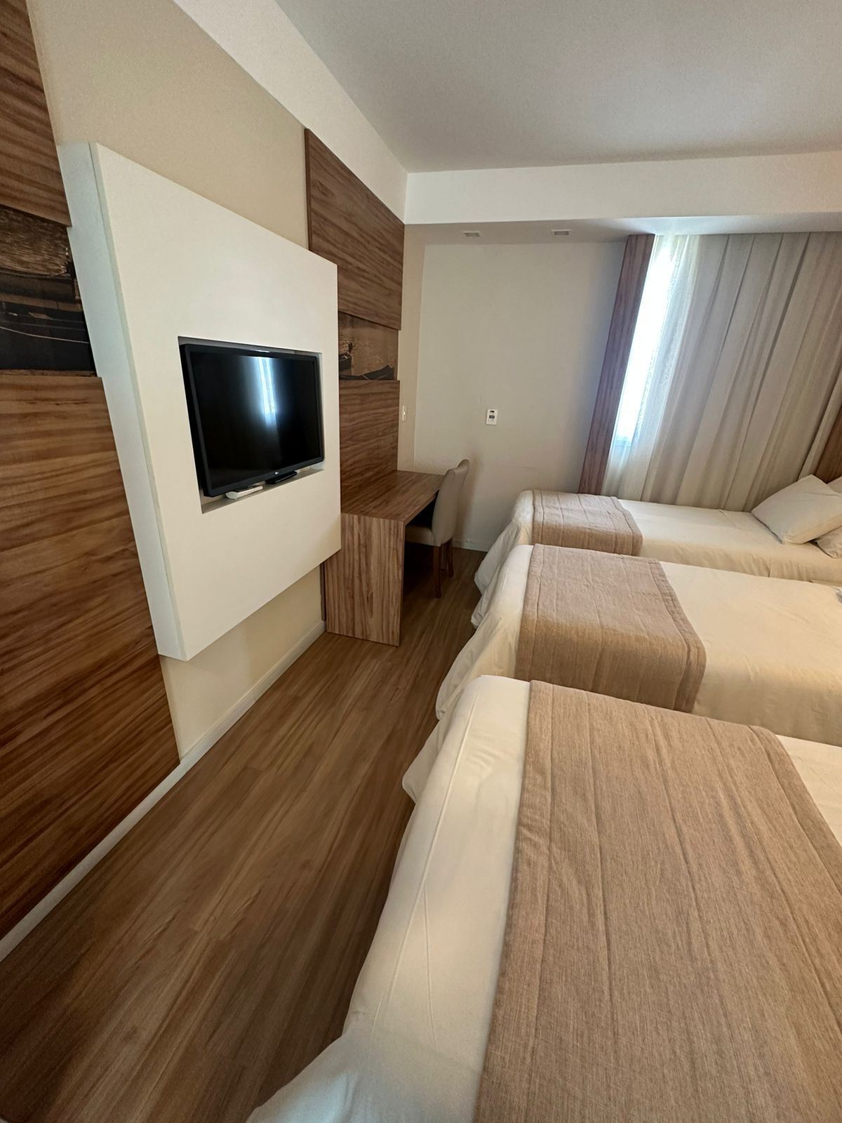 Habitación de hotel con televisión montada en la pared, un escritorio y tres camas.