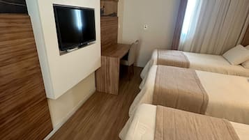 Habitación de hotel con televisión montada en la pared, un escritorio y tres camas.