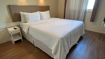 Un dormitorio ordenado con una cama grande, mesitas de noche y una ventana con cortinas.