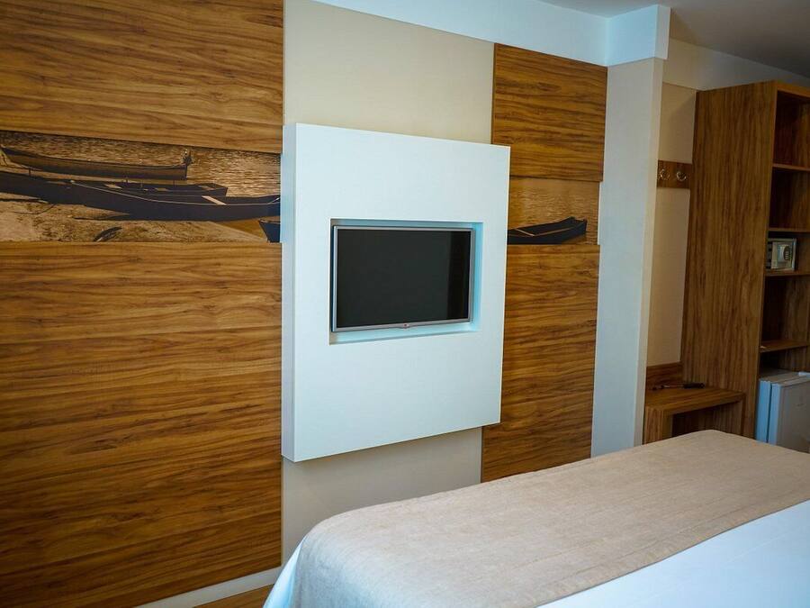 A modern room with a bed, a mounted TV, wooden panel walls, and a built-in bookshelf.