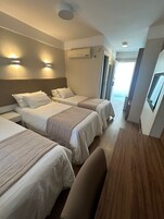 Quarto de hotel com três camas, uma escrivaninha e vista para o mar.