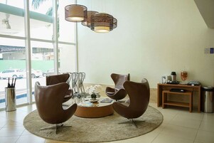 Um interior moderno com duas cadeiras marrons em torno de uma mesa redonda, um lustre e vista para carros estacionados lá fora.