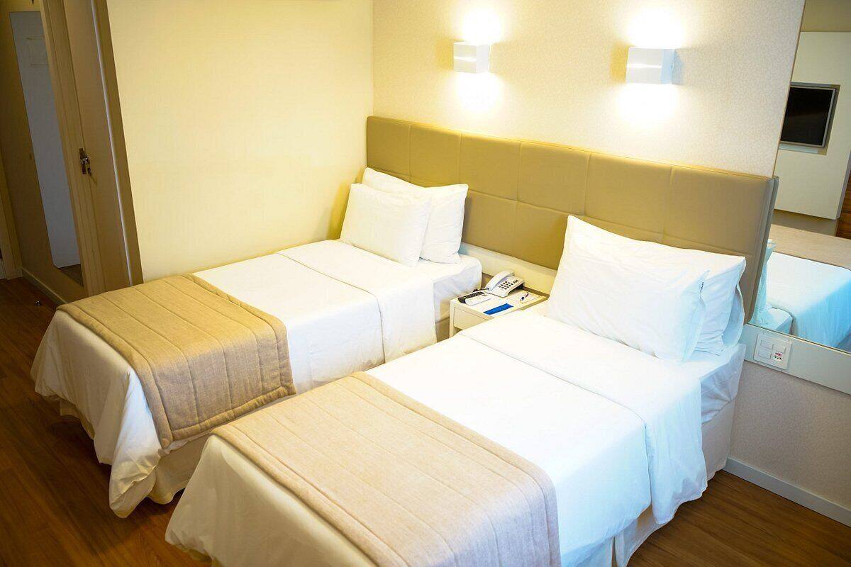 A hotel room with two beds, a bedside table with a phone, and a mirror.