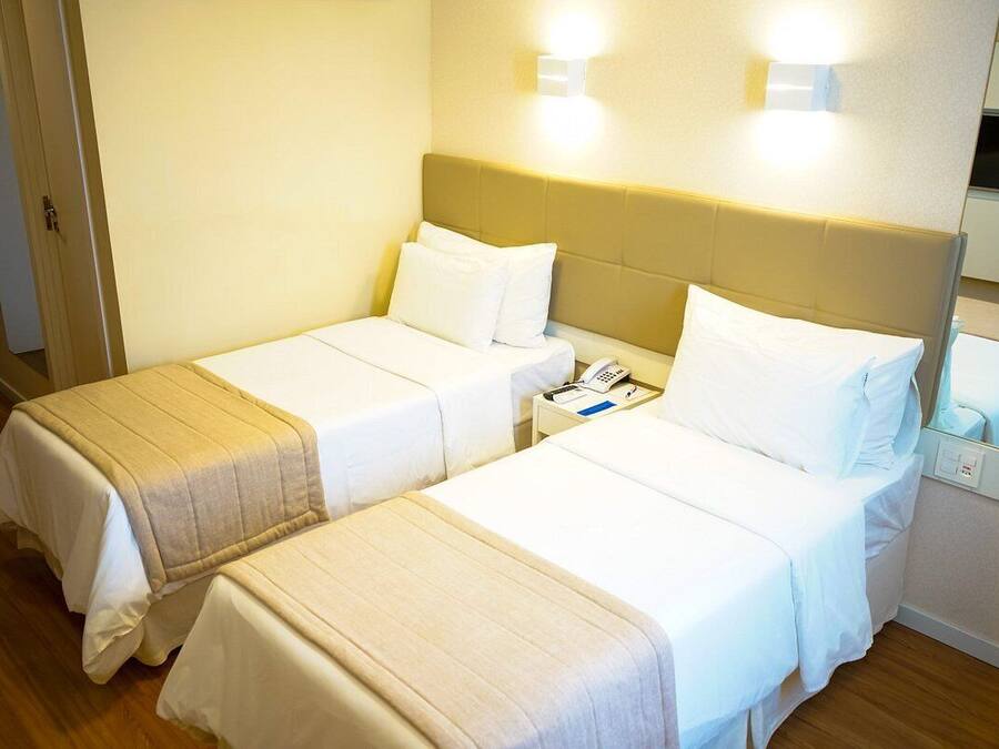 A hotel room with two beds, a bedside table with a phone, and a mirror.