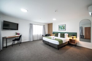 A hotel room with a bed, a desk, a chair, a TV, a bedside table with a lamp, and a large mirror. - Solsen Flexi Stay & Motel (Auckland)