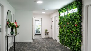 Un pasillo con una pared verde, un espejo, una pequeña mesa con un florero y una puerta al final.