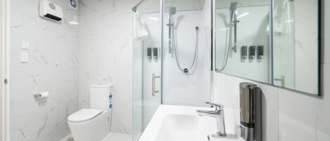 Un baño moderno con ducha de vidrio, lavamanos blanco y retrete.
