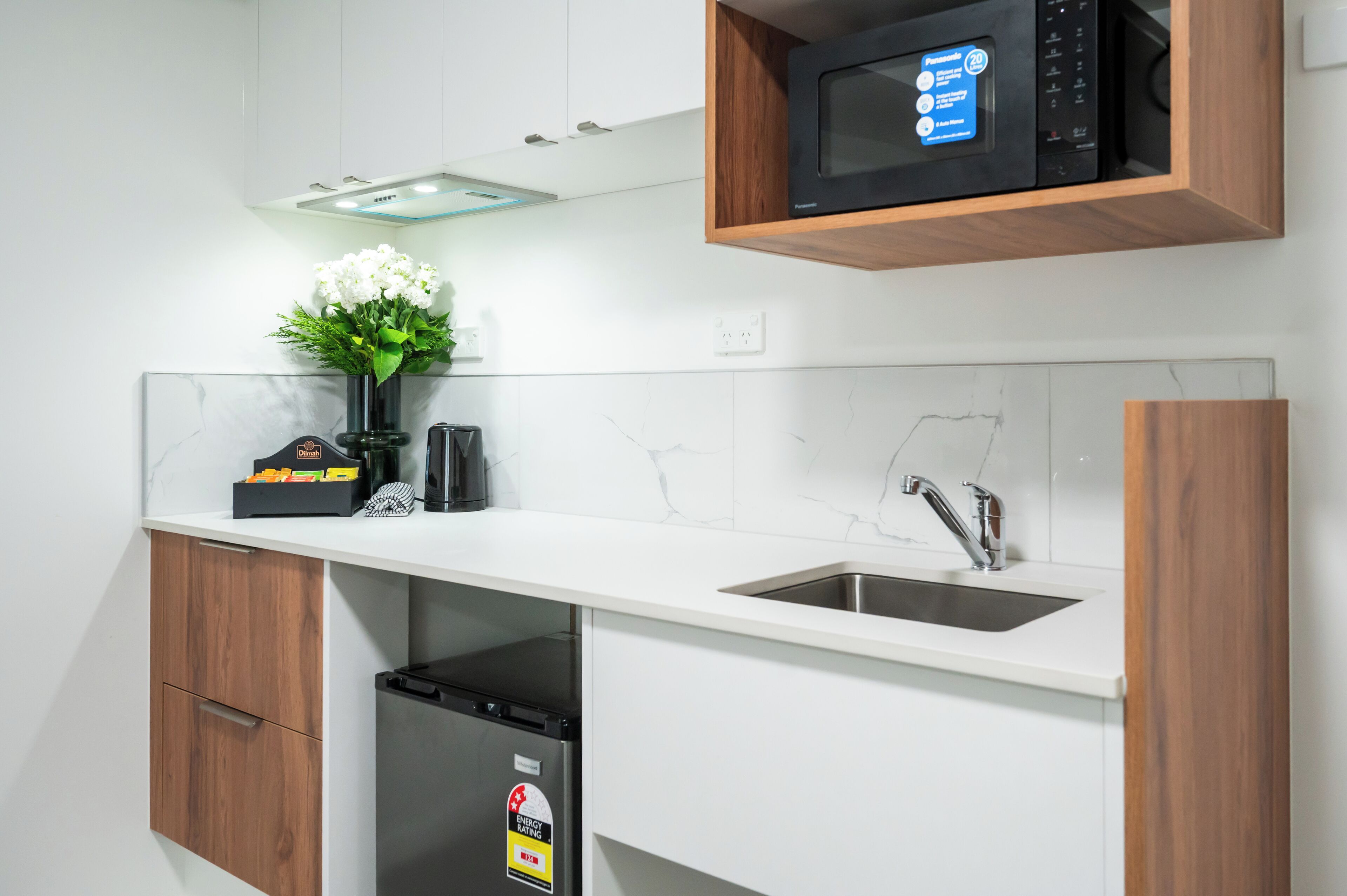 A modern kitchen with white cabinetry, a built-in microwave, a sink, and a dishwasher.
