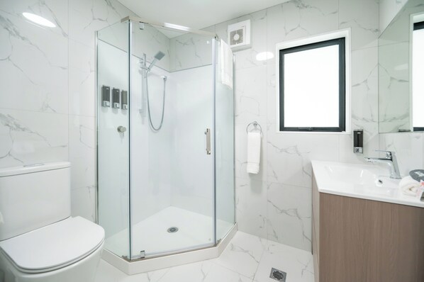 Un baño moderno con ducha envuelta en vidrio, inodoro blanco y lavamanos con espejo superior.