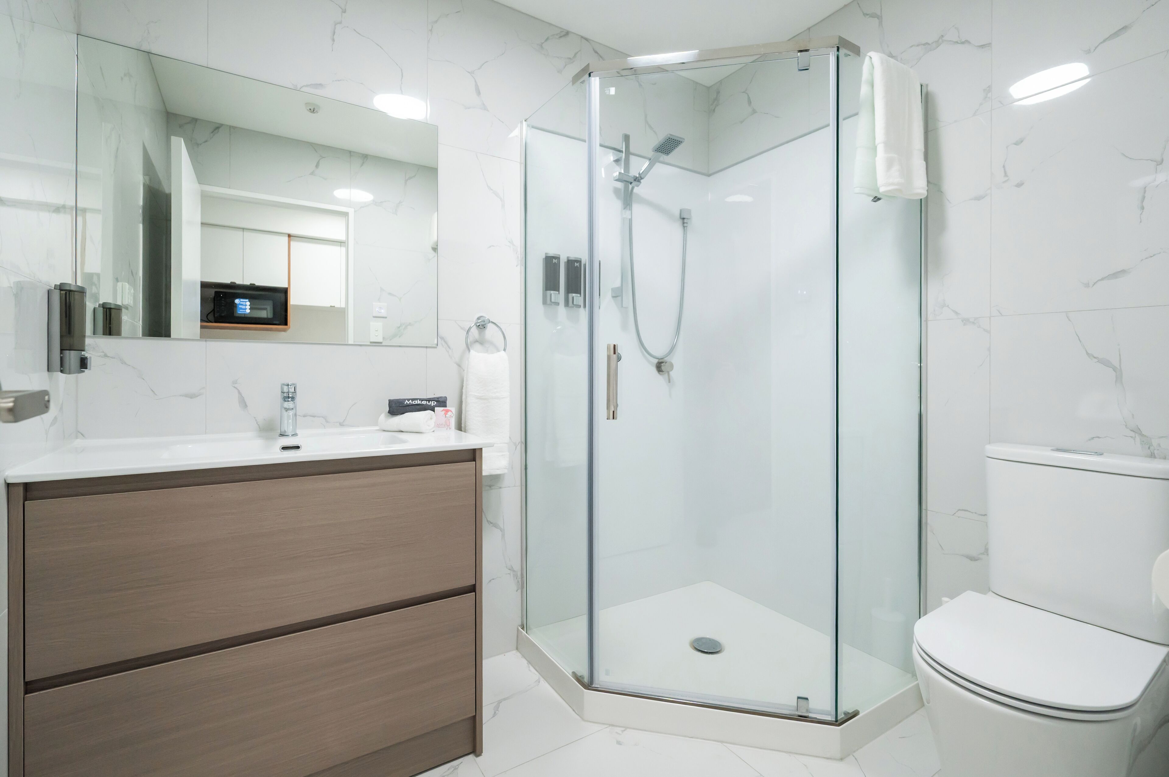 A modern bathroom with a glass-enclosed shower, a toilet, and a vanity with a mirror and a microwave.
