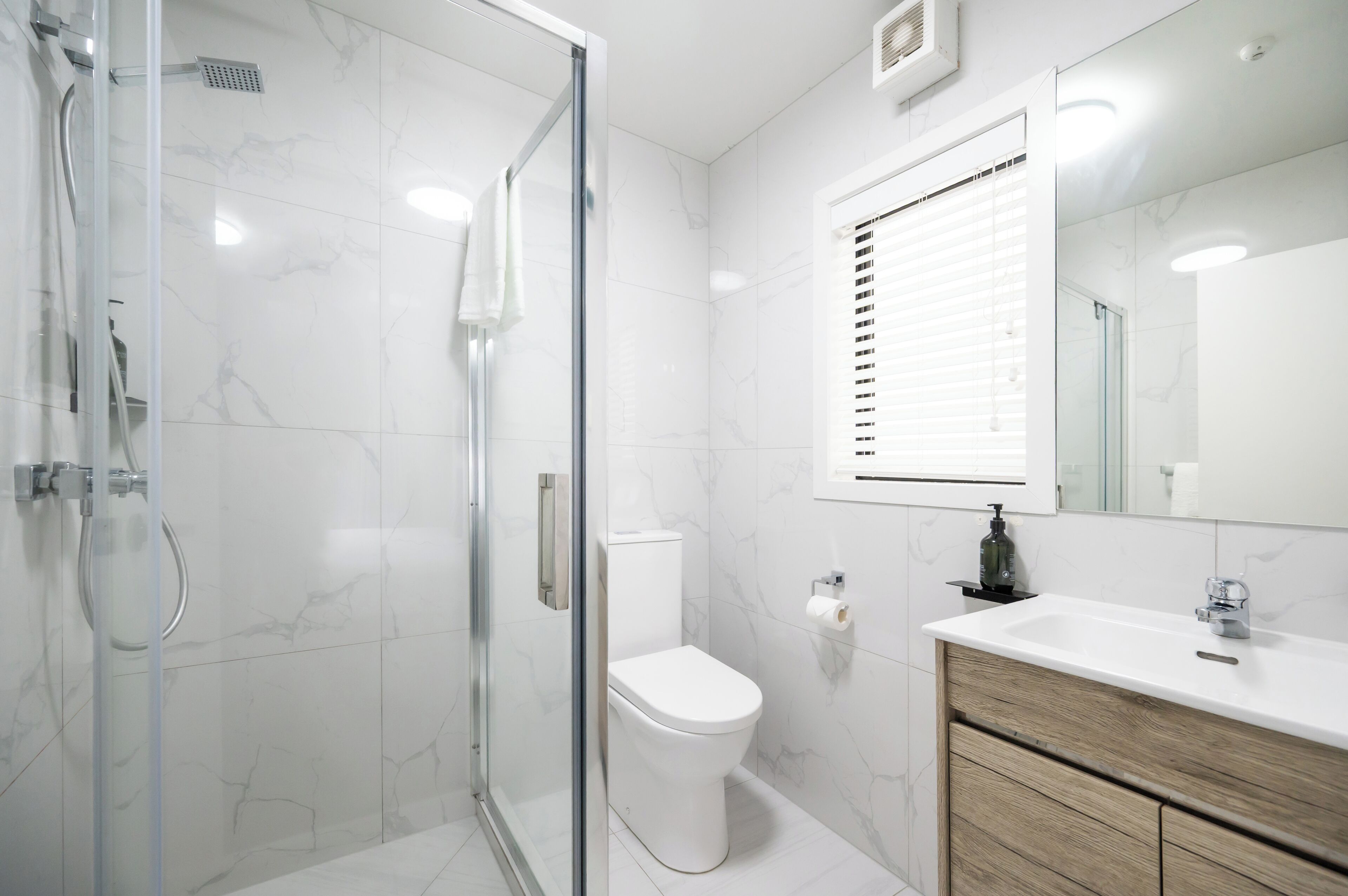 Une salle de bain moderne avec une douche à parois de verre, des toilettes blanches, un meuble-lavabo en bois et un grand miroir.