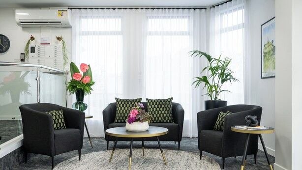 Una habitación de hotel moderna con un sofá negro, una mesita redonda con un centro de flores y una pequeña mesita auxiliar con un objeto decorativo.