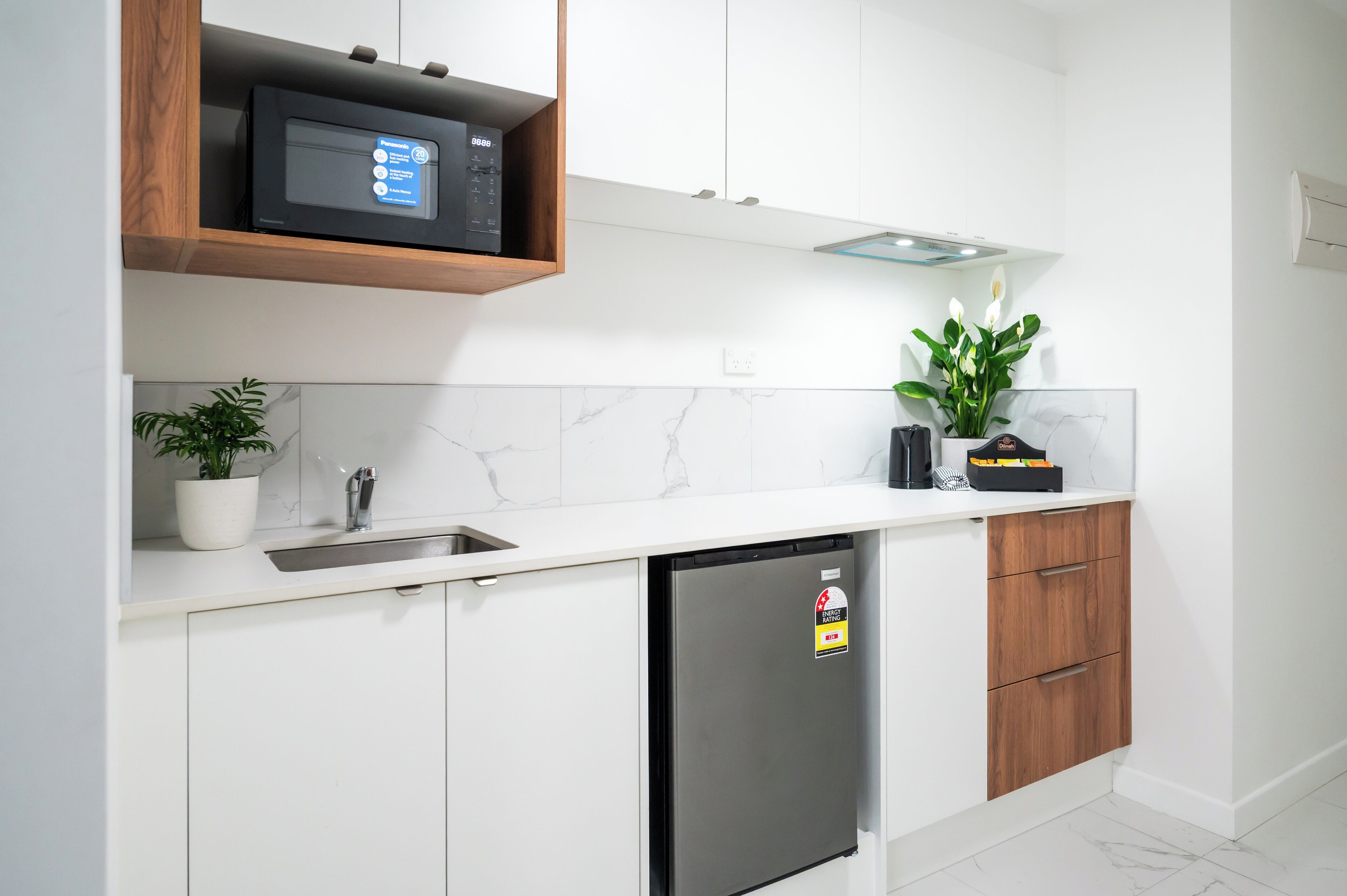 Cozinha moderna com armários brancos, lava-louças de aço inoxidável, micro-ondas e um vaso de planta.
