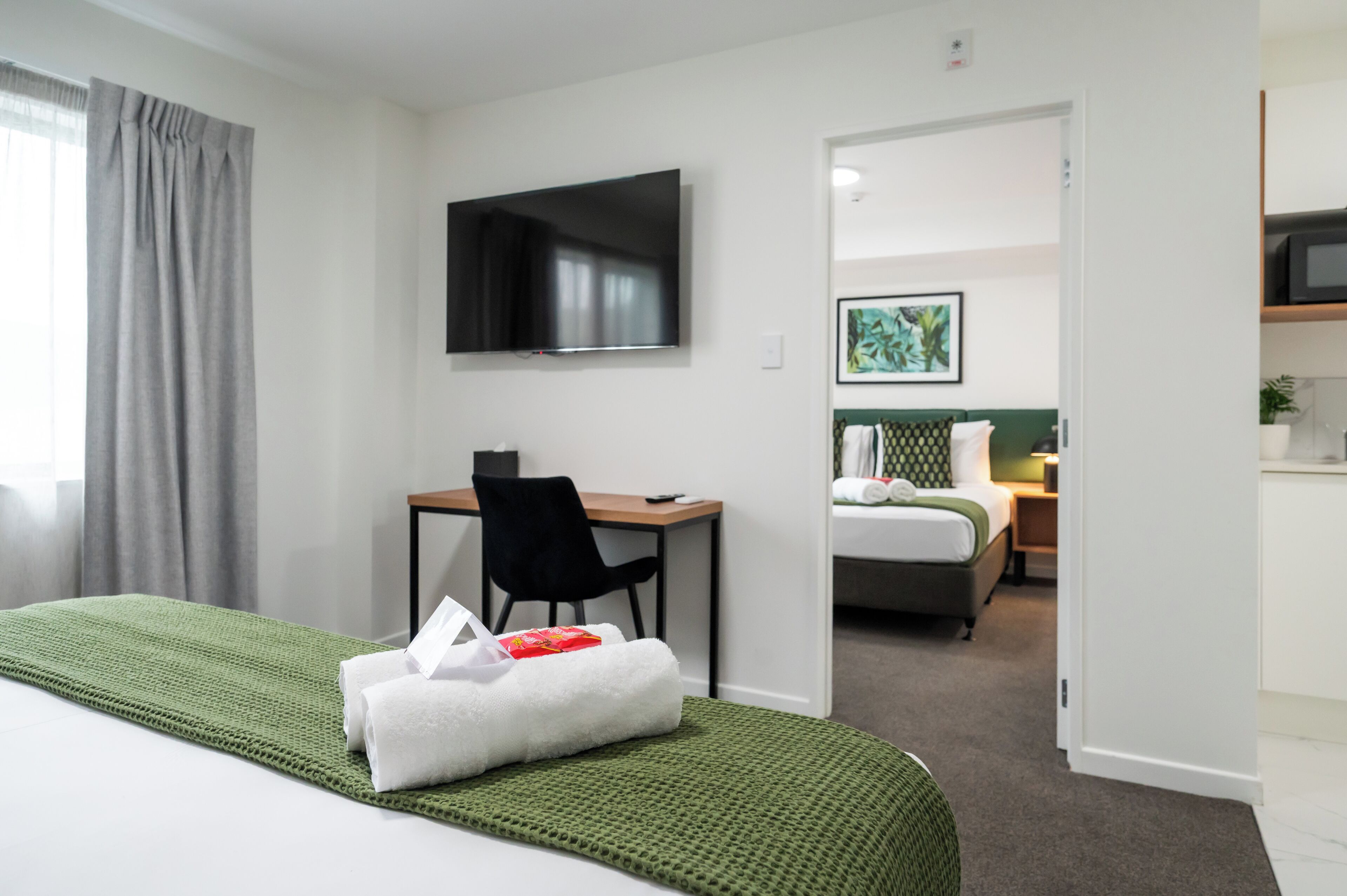 Habitación de hotel con cama, escritorio, silla, televisor y un cuadro en la pared.