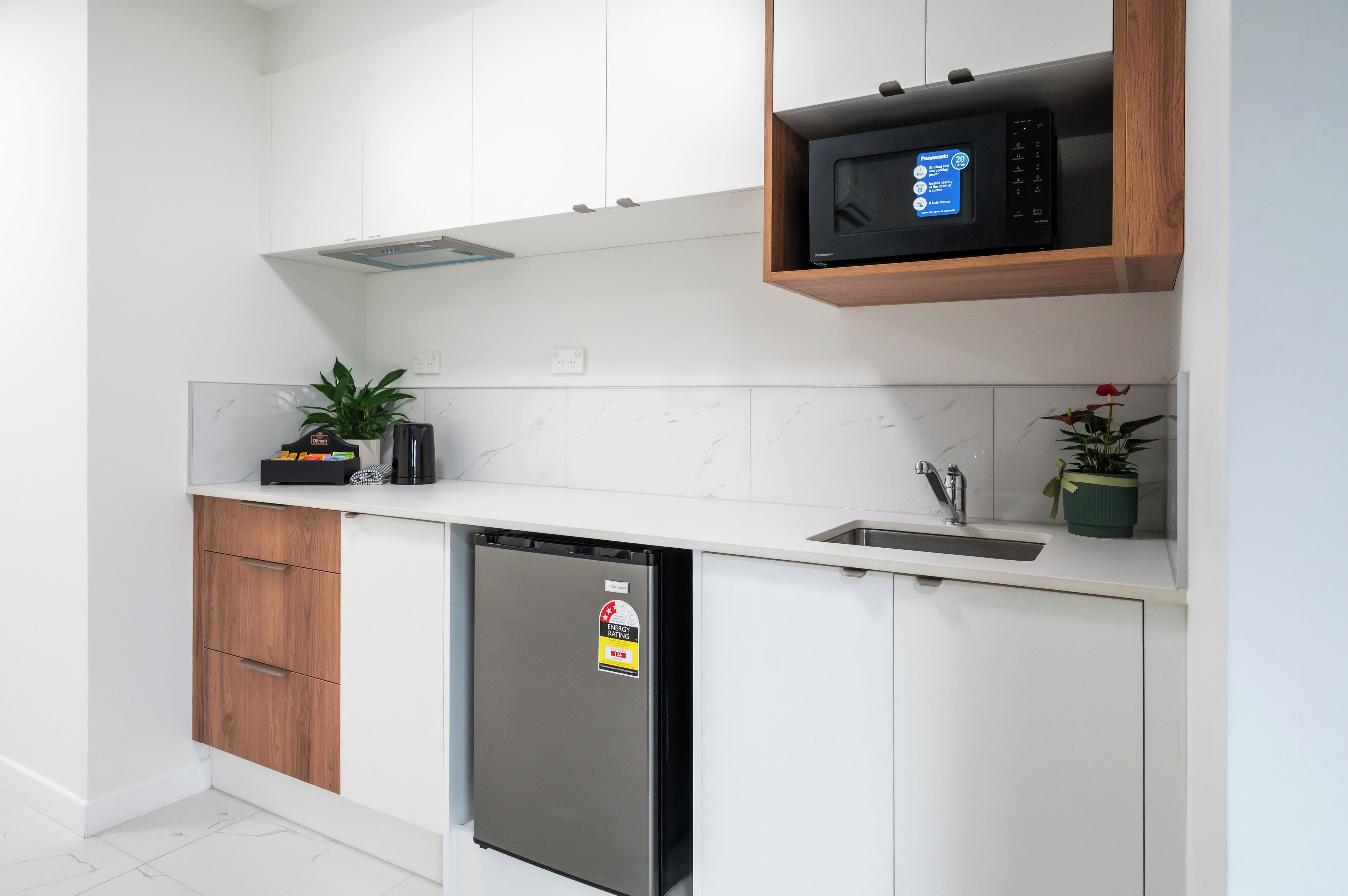 A modern kitchen with white cabinets, a built-in microwave, a dishwasher, and a small sink.