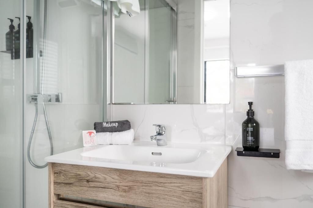 Un baño moderno con un lavabo blanco, un mueble de tocador de madera, un espejo grande y una zona de ducha.