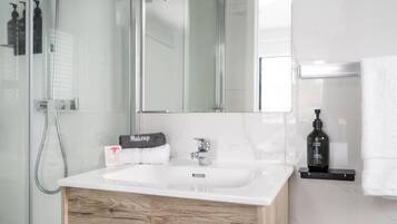 Un baño moderno con un lavabo blanco, un mueble de tocador de madera, un espejo grande y una zona de ducha.