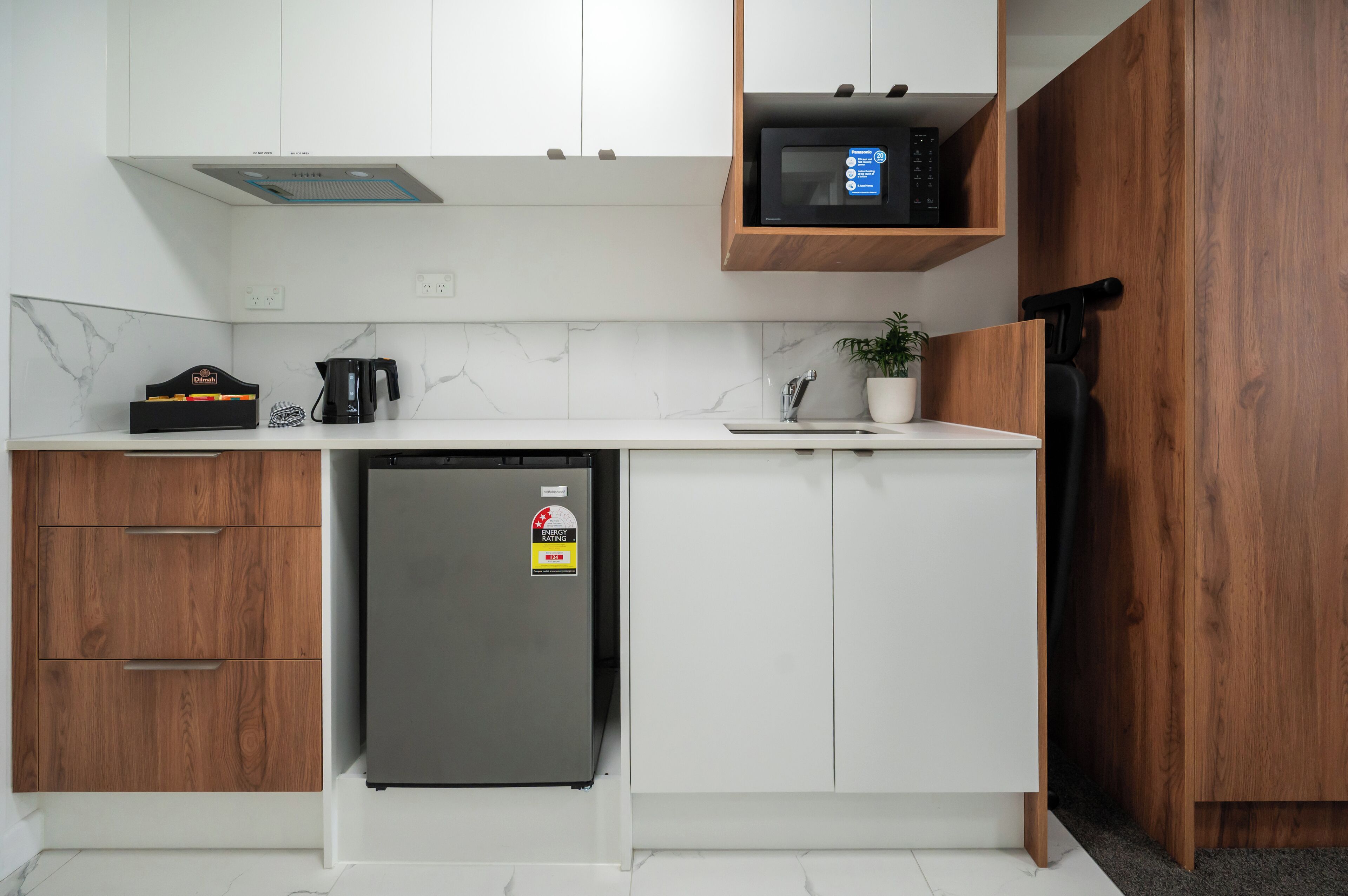 A compact kitchen with white cabinets, a built-in microwave, a refrigerator, and a coffee maker.